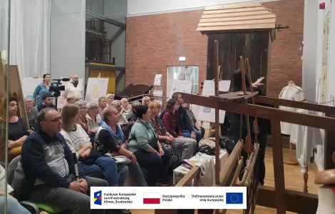 grupa osób oglądających wyświetlaną prezentację, na pierwszym planie duże drewniane krosno