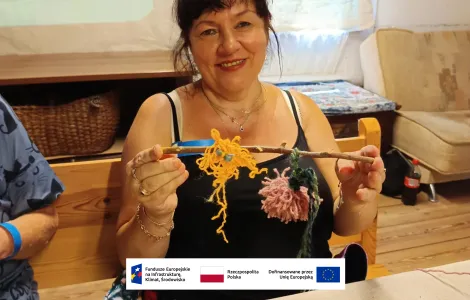 kobieta w średnim wieku z ciemnymi włosami i grzywką - uczestniczka warsztatów prezentująca swoją pracę wykonaną podczas zajęć