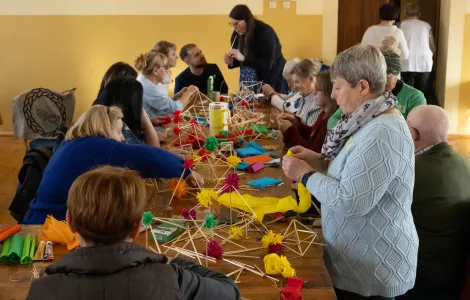 grupa ludzi przy stole warsztatowym tworząca słomkowe pająki