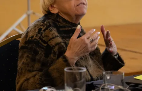 starsza kobieta w okularach z grubymi oprawkami gestykulująca podczas wystąpienia przed uczestnikami wydarzenia