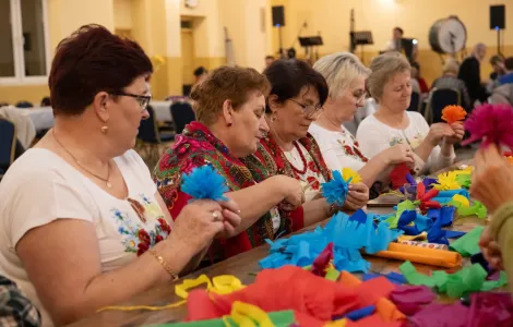 grupa kobiet siedząca przy stole i tworząca kolorowe kwiaty z bibuły 