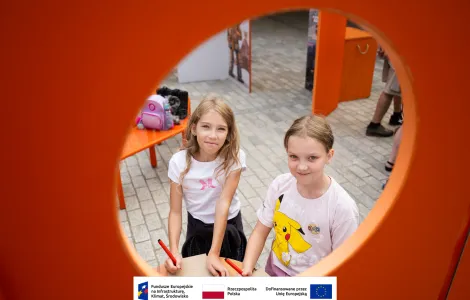 Dwie dziewczynki w wieku szkolnym trzymające kartki oraz pisaki podczas zajęć towarzyszących otwarciu wystawy. 