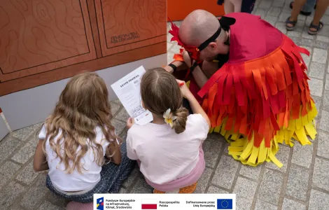 Mężczyzna przebrany za feniksa oraz dwie dziewczynki podczas rozwiązywania quizu 