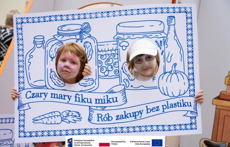 Dwie dziewczynki z pomalowanymi twarzami w monidle stylizowanym na starodawną makatkę z napisem „fiku miku, rób zakupy bez plastiku”