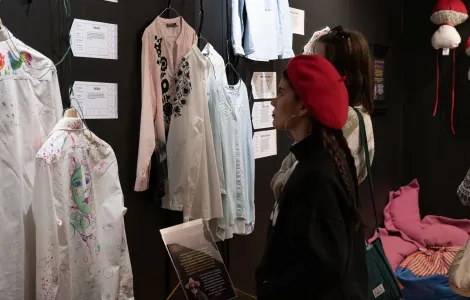 młoda kobieta z ciemnymi włosami w czerwonym berecie podziwiająca zawieszone na ścianie tekstylne eksponaty