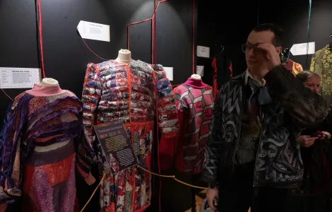 młody mężczyzna w okularach przechadzający się wśród manekinów ubranych w ekscentryczne stroje wykonane z plastikowych elementów 