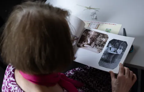 Siedząca tyłem kobieta ogląda album z czarno - białymi zdjęciami. Zdjęcia są stare.