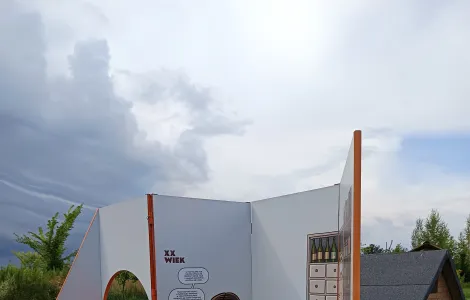 jedna ze ścianek wystawy mobilnej, na której znajduje się sylwetka wąsatego sklepikarza, w tle pochmurne niebo 