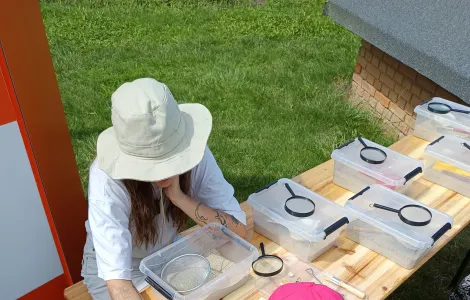 Młoda kobieta w kapeluszu oraz dziewczynka w różowej czapce siedzące przy drewnianym stole i rozwiązujące jakiś rebus