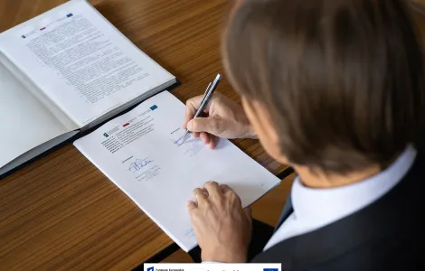 mężczyzna z ciemnymi włosami podpisujący leżący przed nim na stole dokument